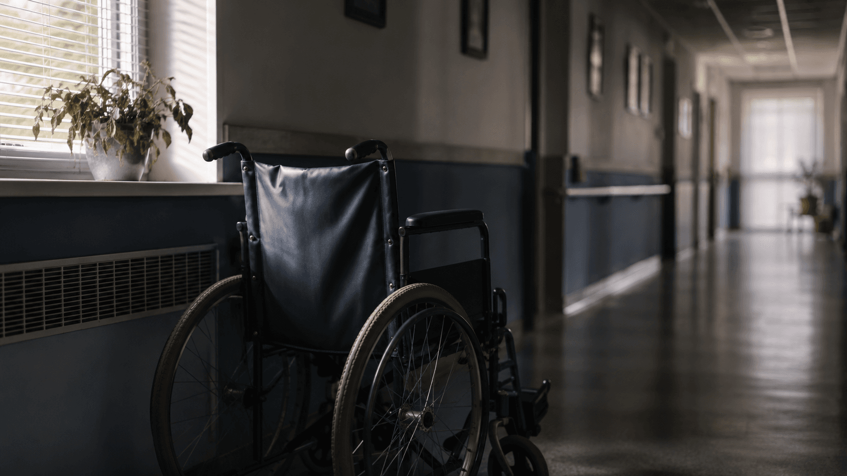 Empty wheelchair beside a window in a quiet nursing home corridor